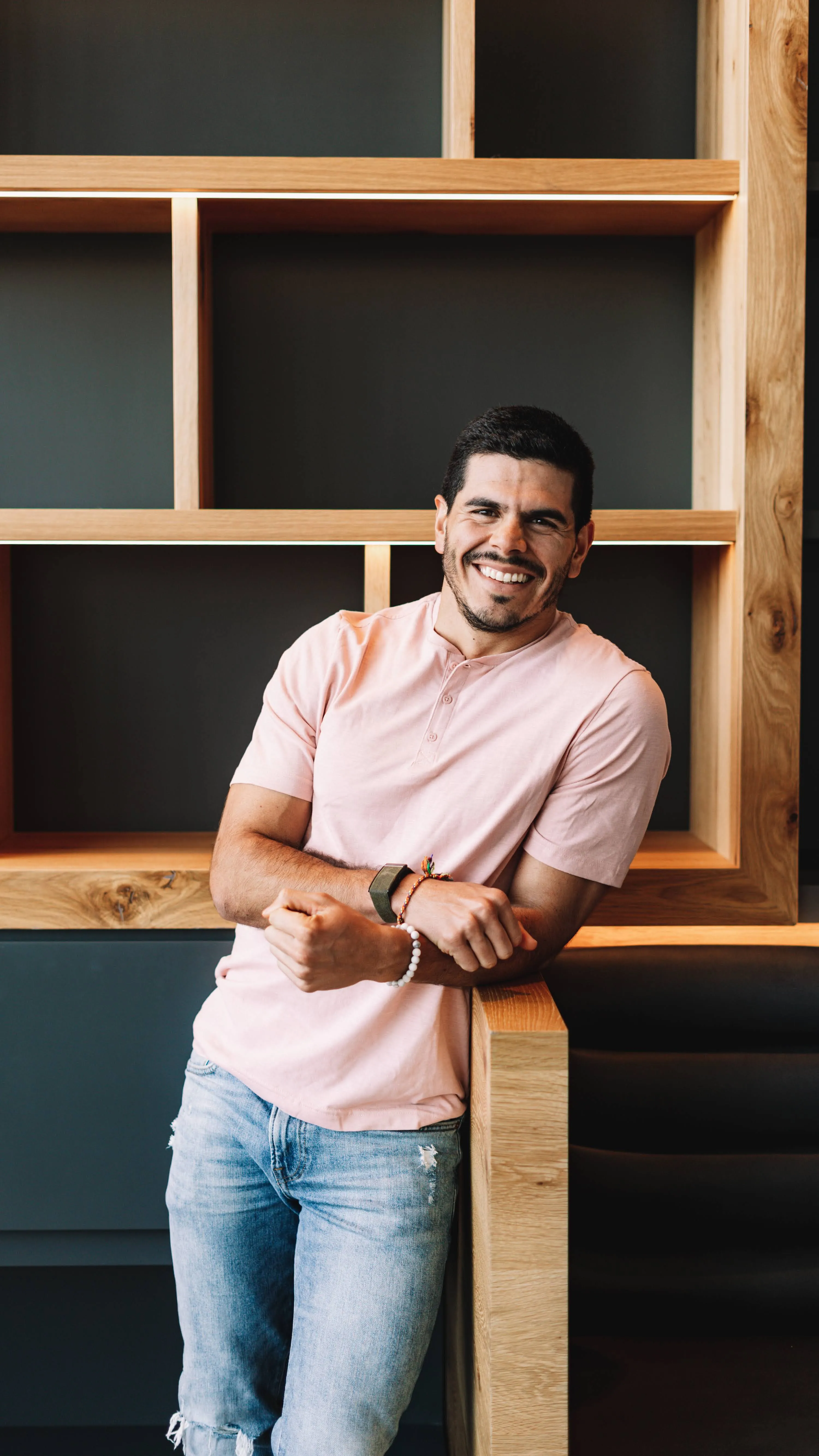 Andres Ayesta smiling, leaning on a wooden shelf